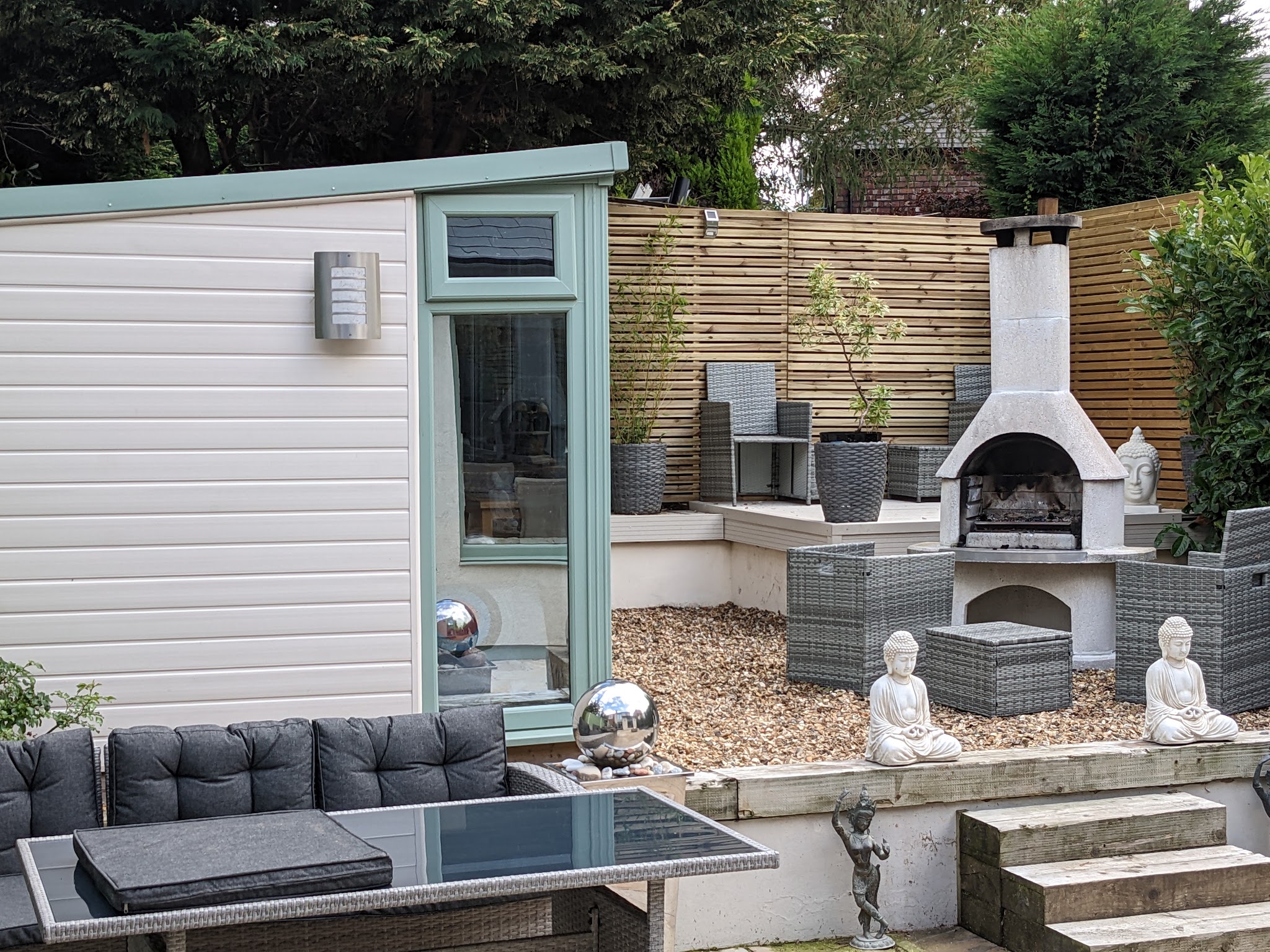 A garden room with a glazed door beside a patio with seating and an outdoor fireplace