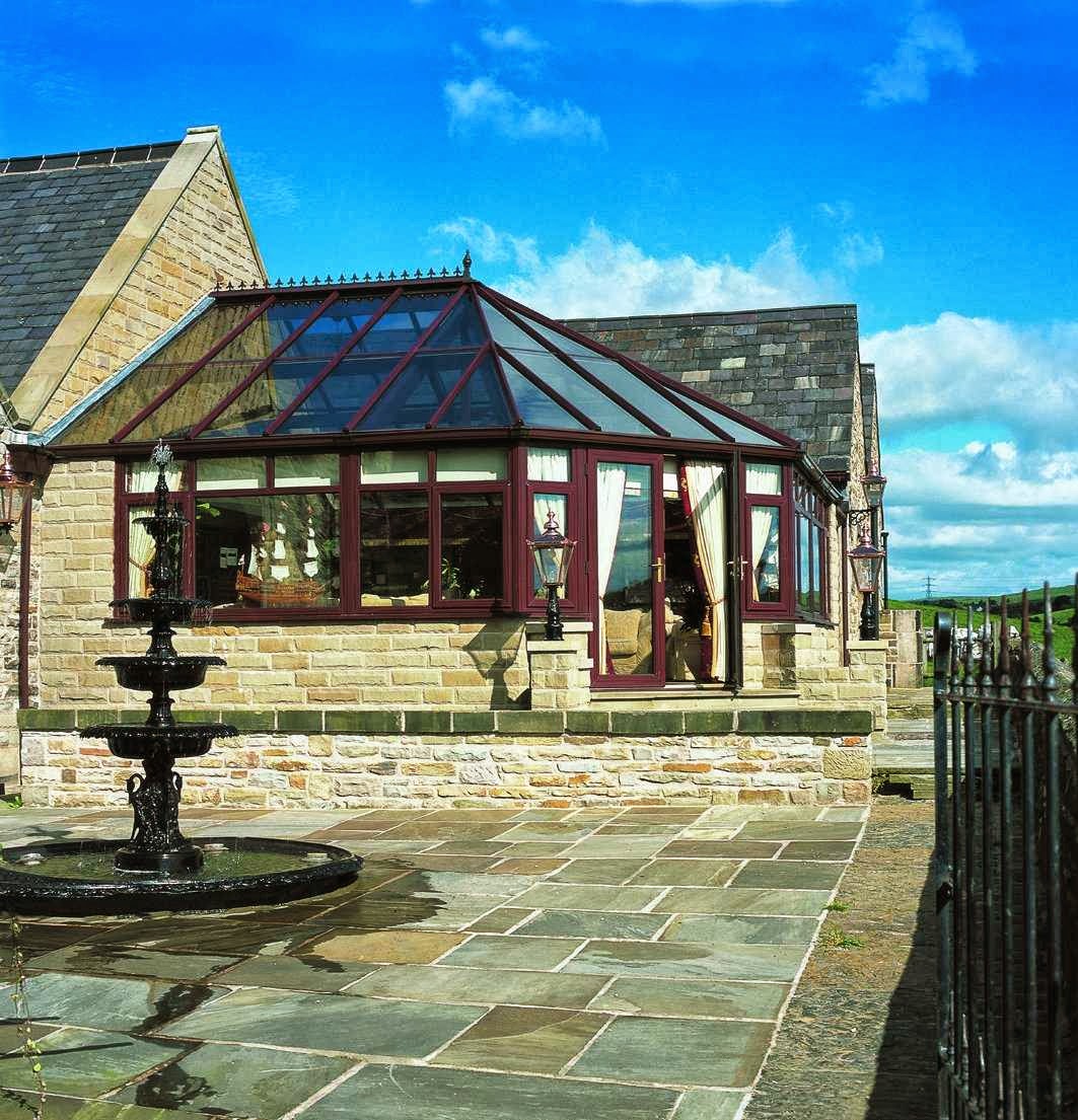 A hipped conservatory with dark red frames on a stone building beside a flagged courtyard